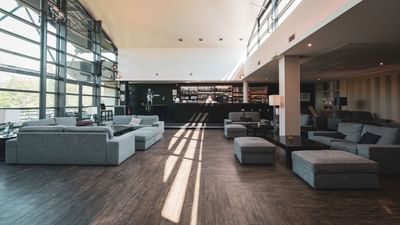 Large lounge area with multiple gray couches, wooden floors, and a bar in the background.