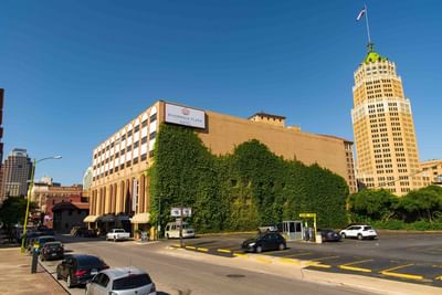 Exterior view of The Riverwalk Plaza Hotel covered in greenery with the city skyline and clear sky
