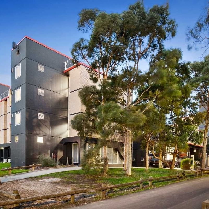 Modern building with red accents and trees on a quiet street at La Trobe University – Menzies College.