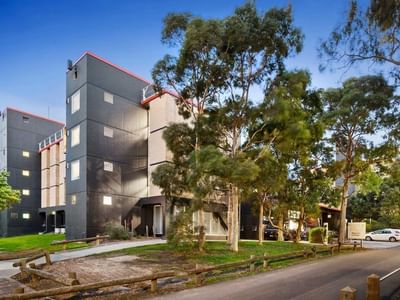 Modern building with red accents and trees on a quiet street at La Trobe University – Menzies College.
