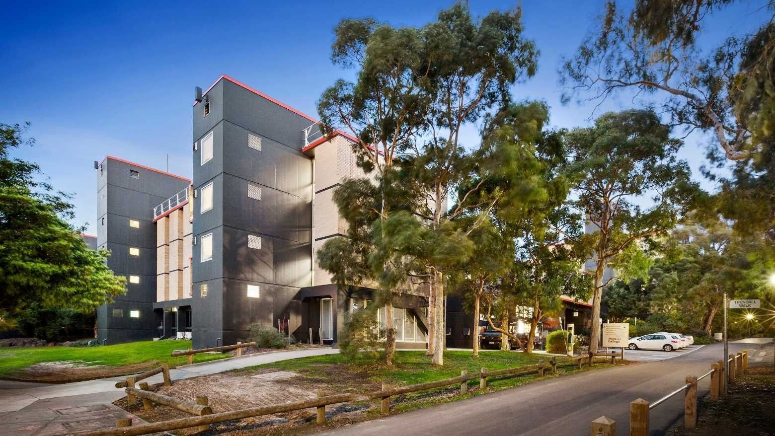 Modern building with red accents and trees on a quiet street at La Trobe University – Menzies College.