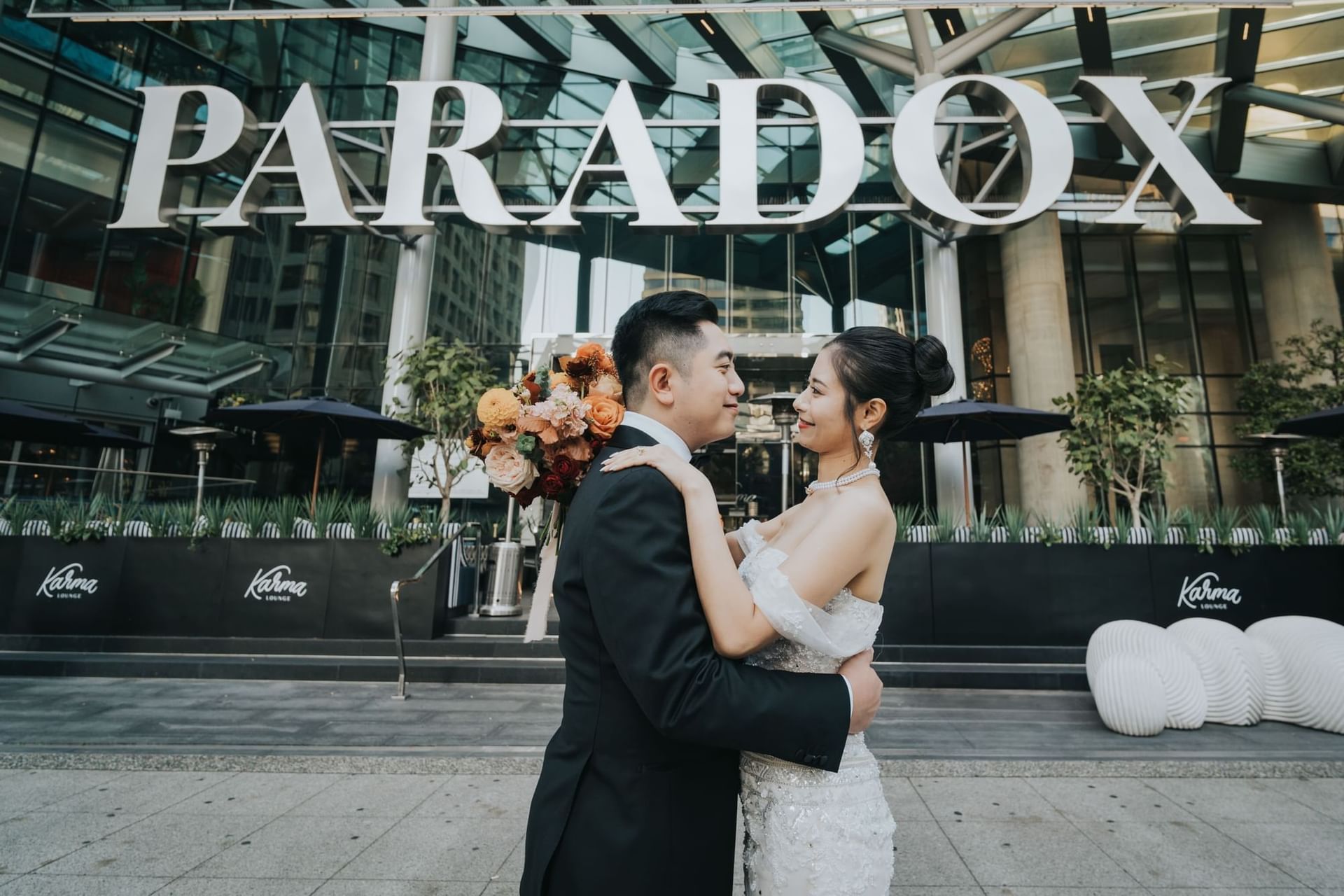 Bride and groom embrace outside the Paradox Vancouver building with Karma Lounge below.