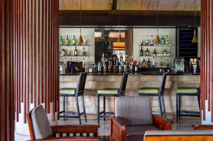 A well-stocked bar with numerous liquor bottles and stools at Warwick Le Lagon - Vanuatu.