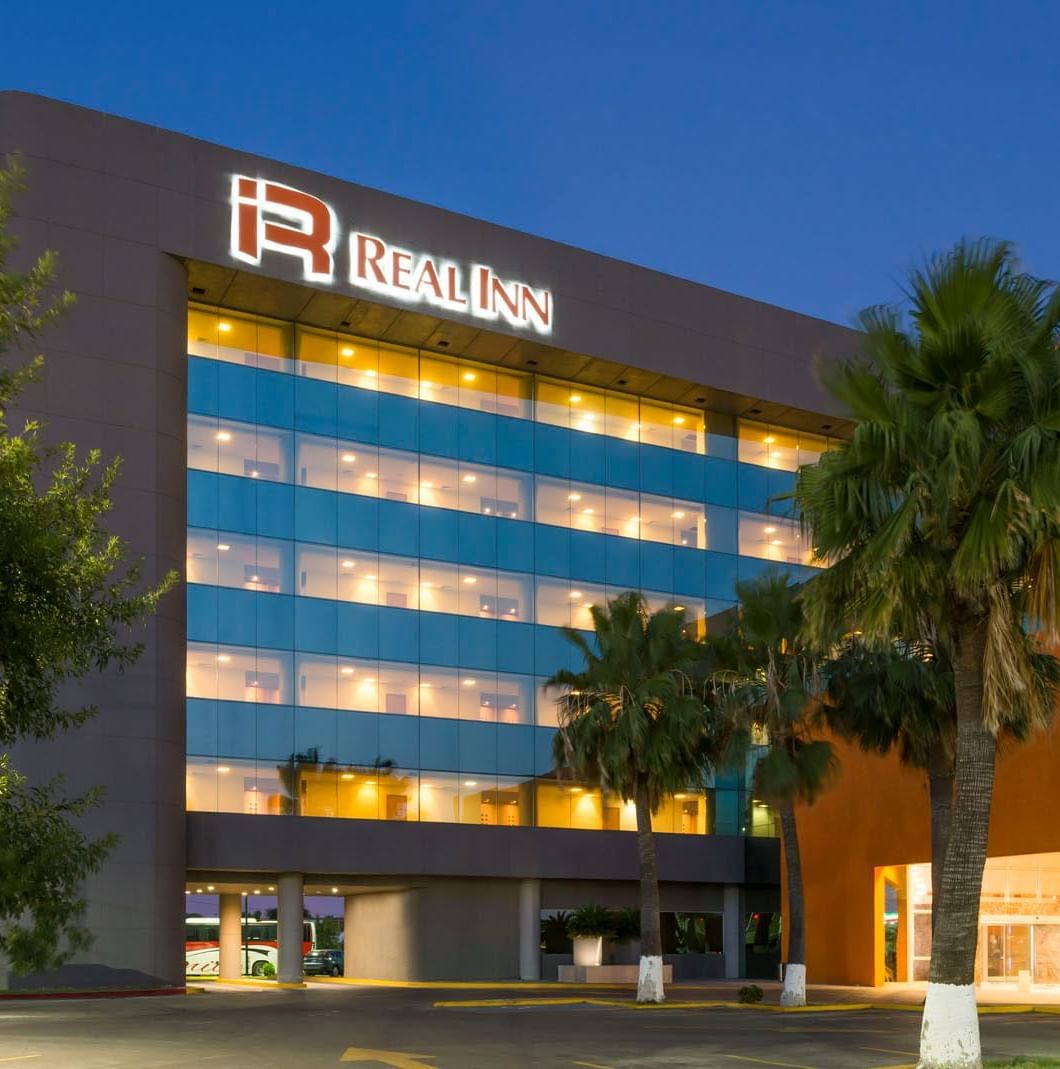 Evening view of the Real Inn Nuevo Laredo exterior, showcasing the illuminated facade and surrounding palm trees
