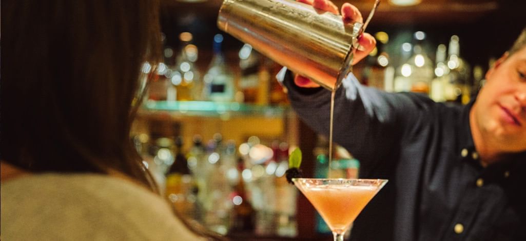 A bartender pours an elegant cocktail for a customer at the bar.