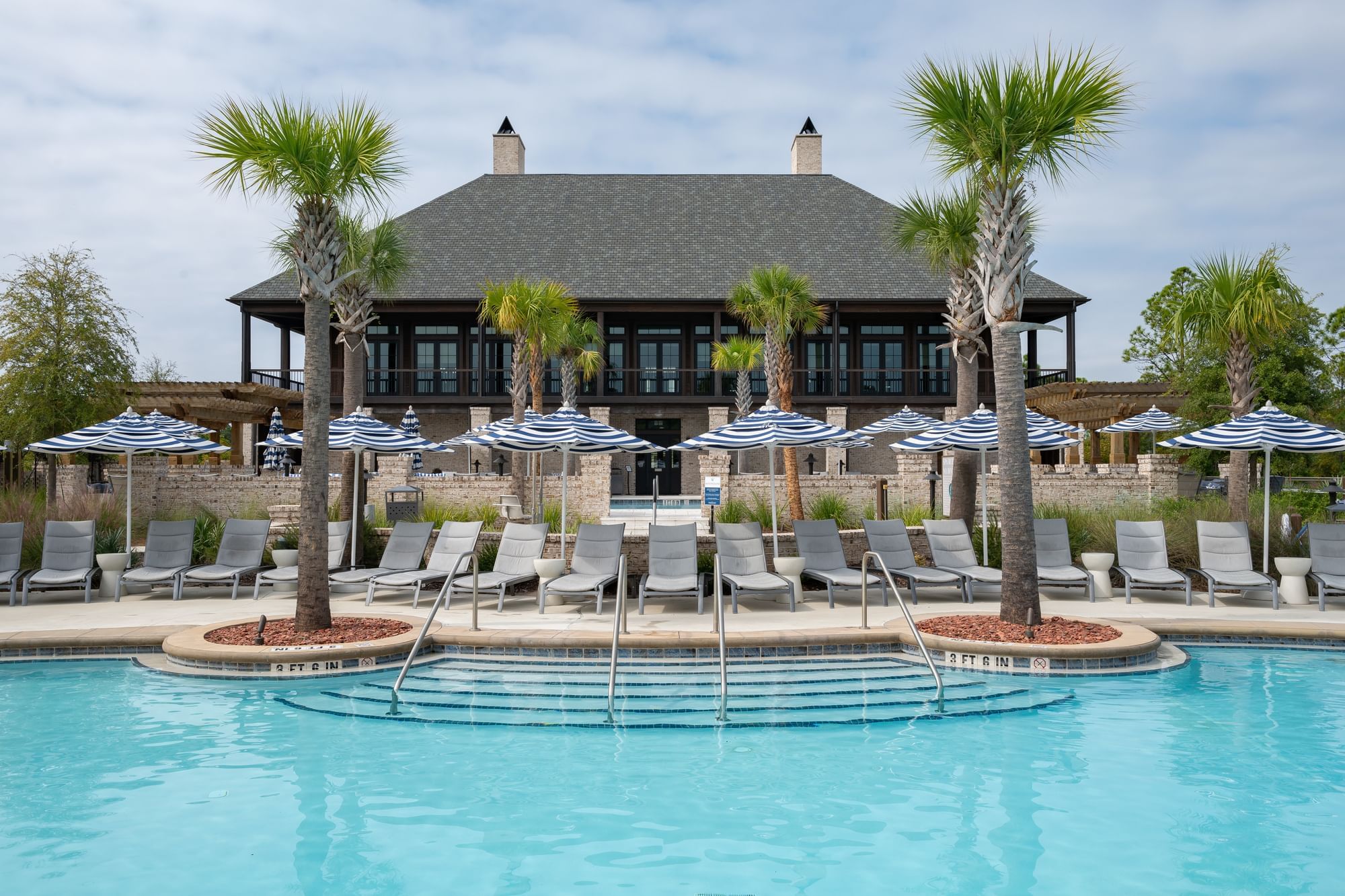 Resort pool with lounge chairs, umbrellas, and palm trees against a building with balconies.