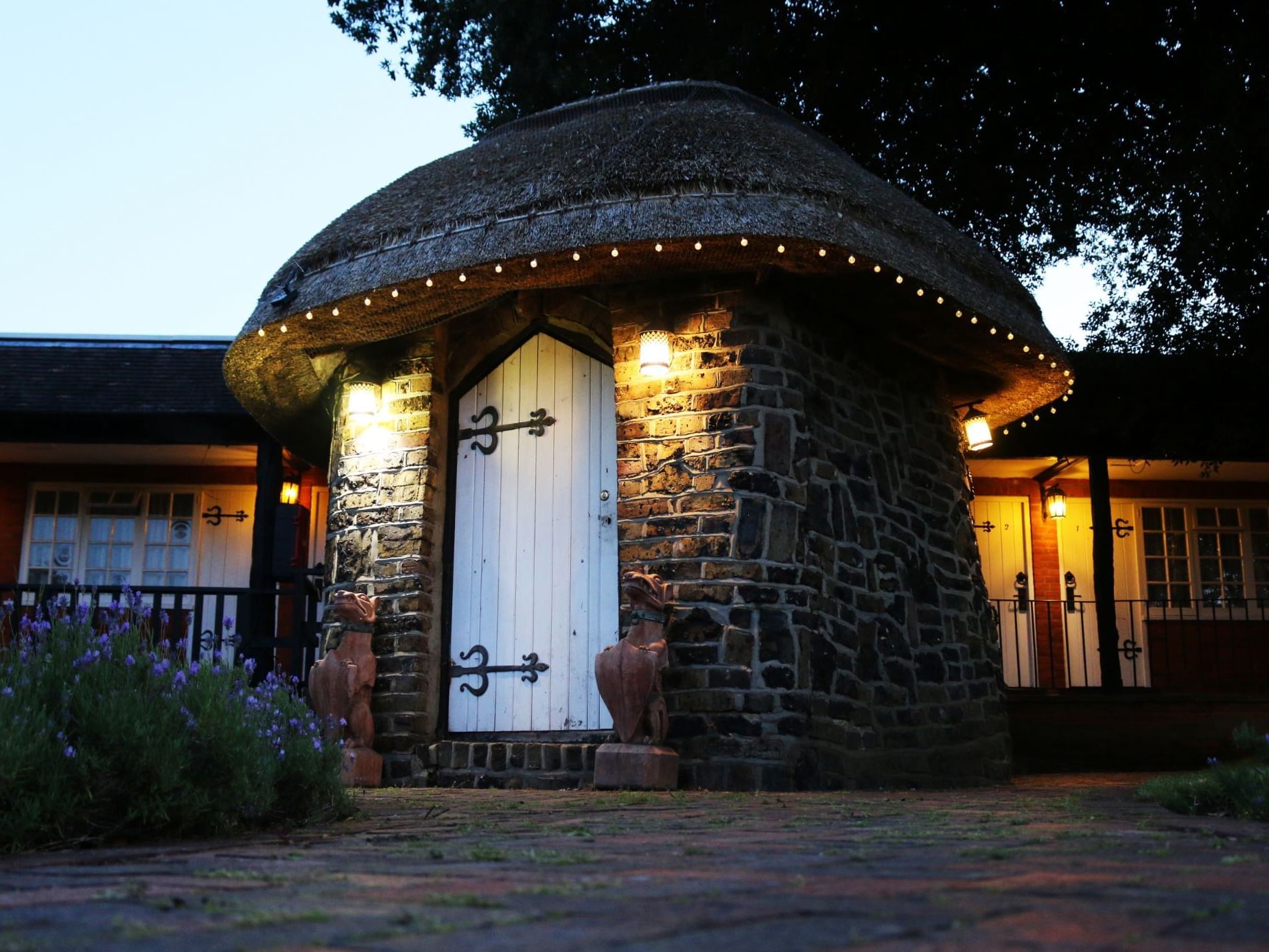 Charming stone-walled building with a thatched roof near Marygreen Manor, illuminated by string lights at dusk