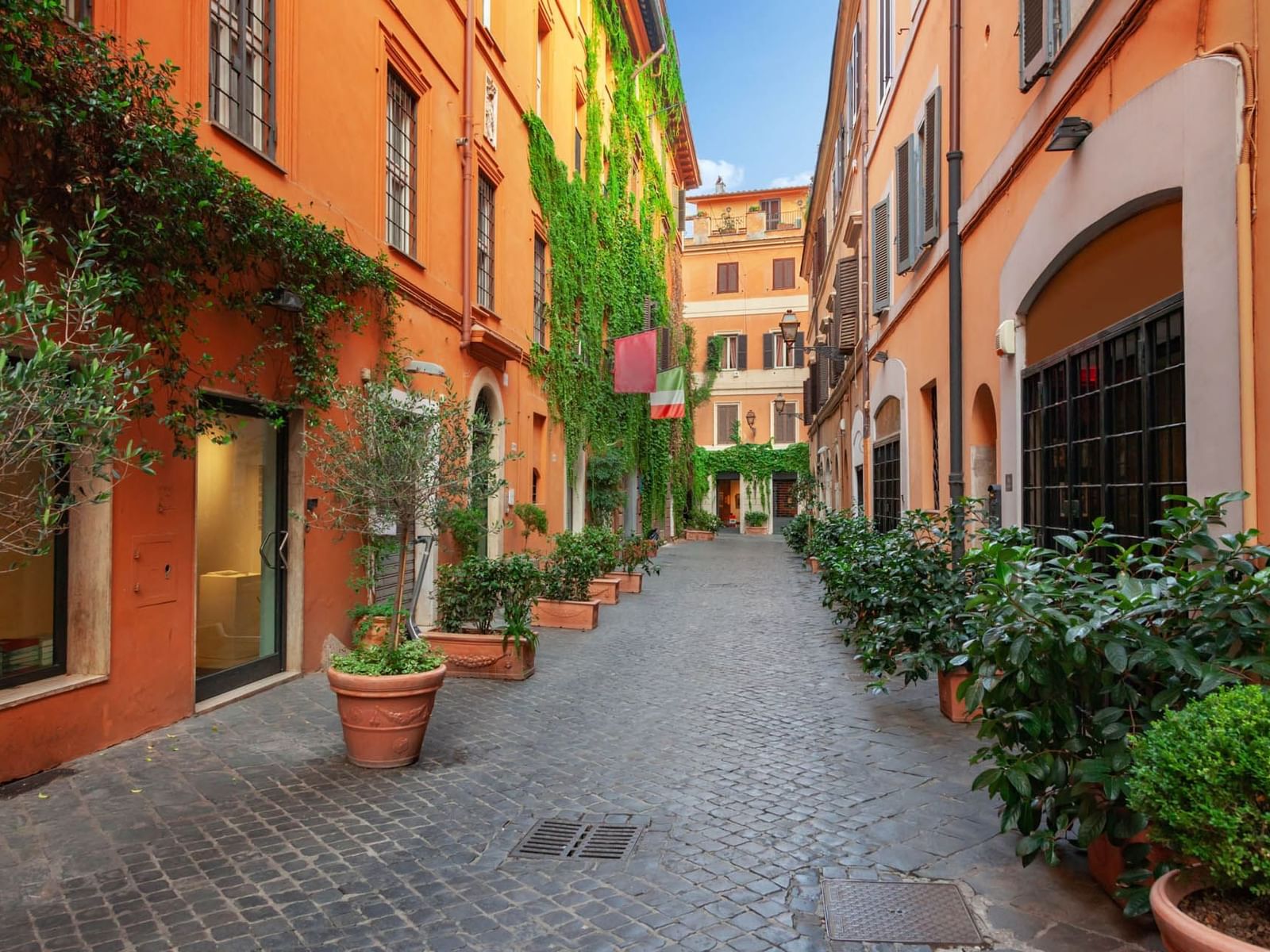 Via Margutta street, lined with orange buildings, greenery, and potted plants near The Glam Hotel