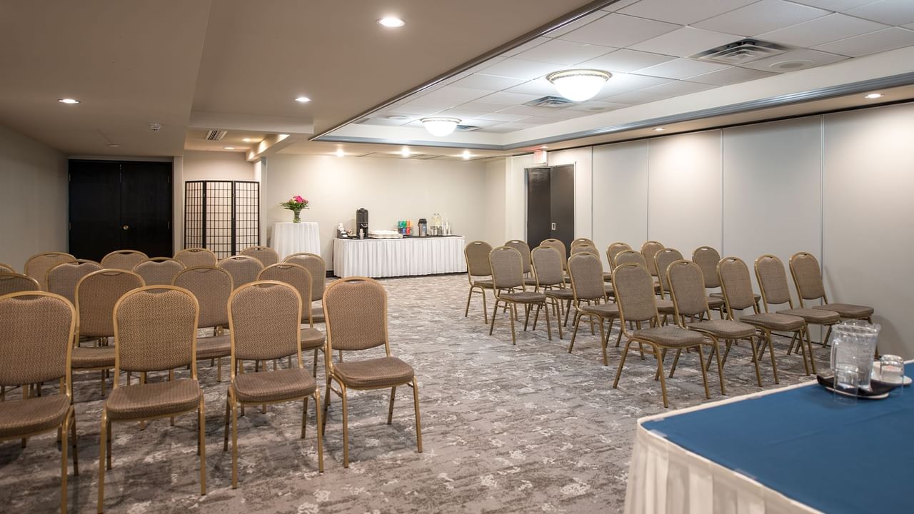 Conference room with chairs, tables, and a stage, with a table set up for refreshments.