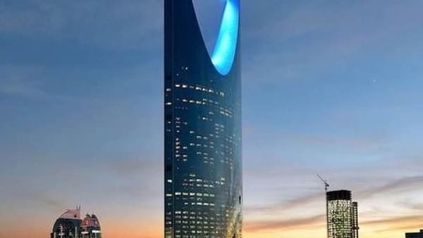 La tour Kingdom Centre, dont l'entrée est éclairée de bleu, se détache sur la silhouette de la ville au crépuscule, près de l'hôtel Cantonal by Warwick Riyadh