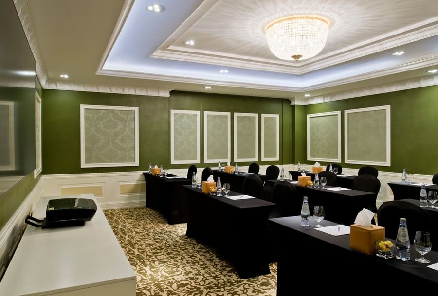 Emerald Room features black chairs by long tables under a crystal chandelier by green walls at Warwick Doha Hotel