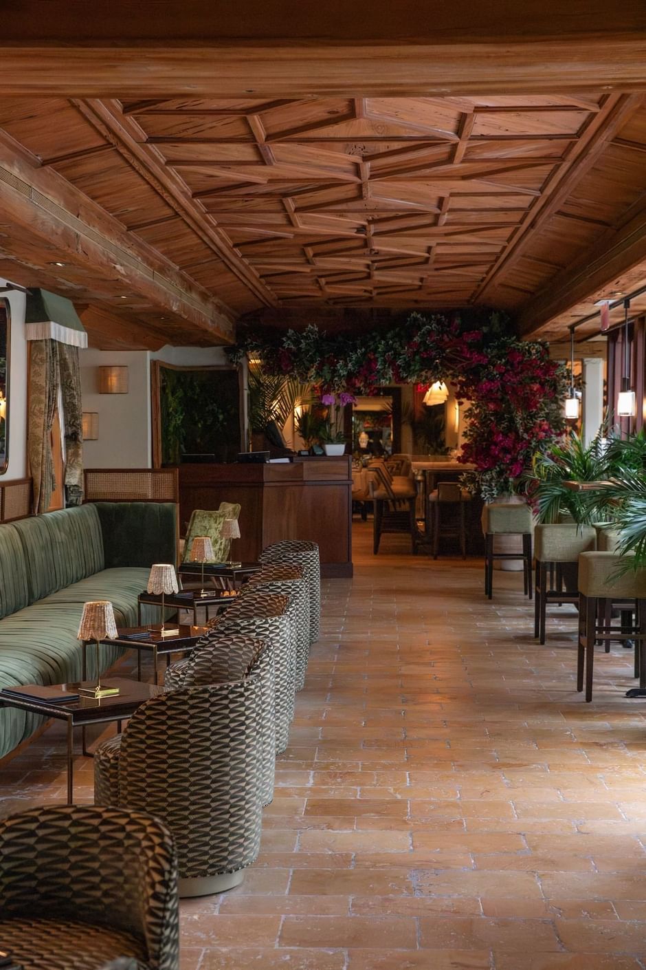 Lobby lounge with wooden ceiling, brick floor, green couch, chairs, and flowers..  