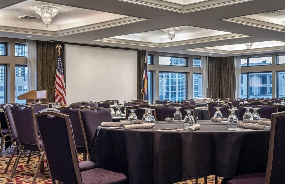 Round tables by purple chairs under crystal chandeliers near a white screen at Warwick Denver