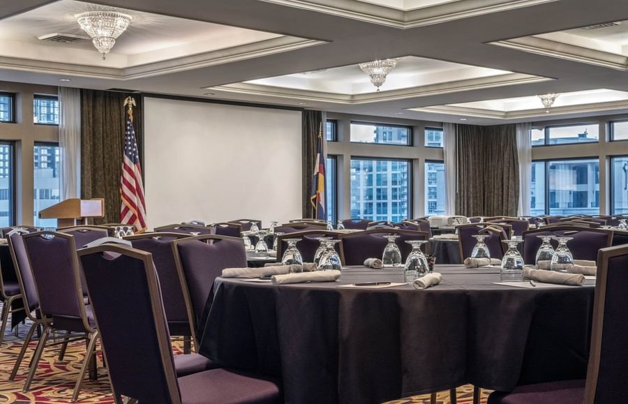 Round tables by purple chairs under crystal chandeliers near a white screen at Warwick Denver