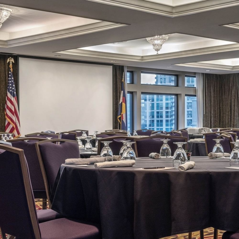 Round tables by purple chairs under crystal chandeliers in Millennium at Warwick Denver