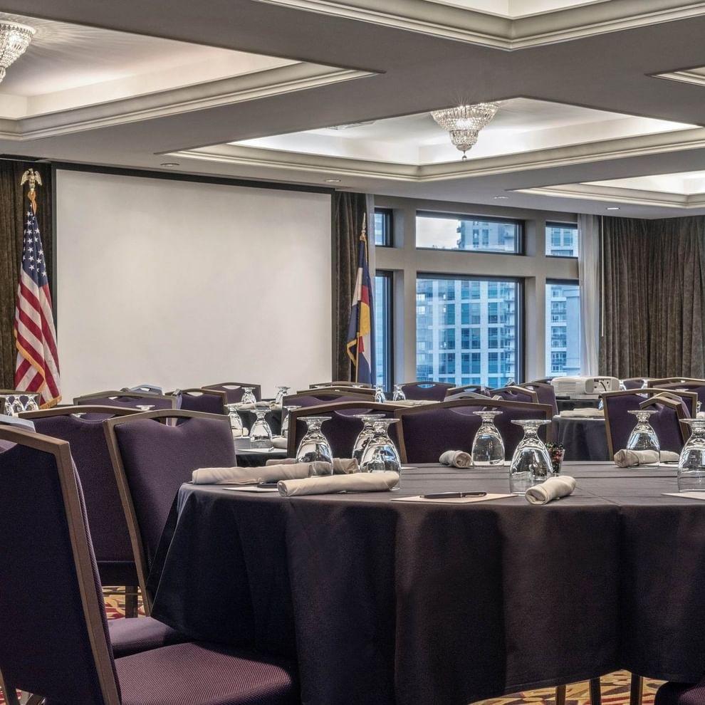 A meeting room with round tables, purple chairs, and a projector screen.