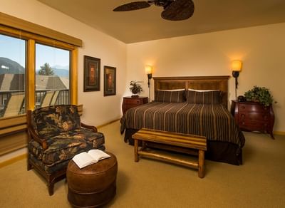 A spacious bedroom with a king-sized bed, dark wood furniture, and a floral armchair at The Stanley Hotel