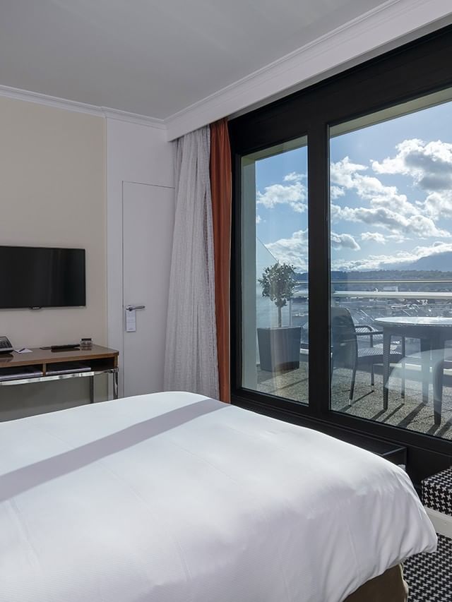 Plush bed by a small desk and floor lamp, facing a terrace in Penthouse Terrace Room at Warwick Geneva