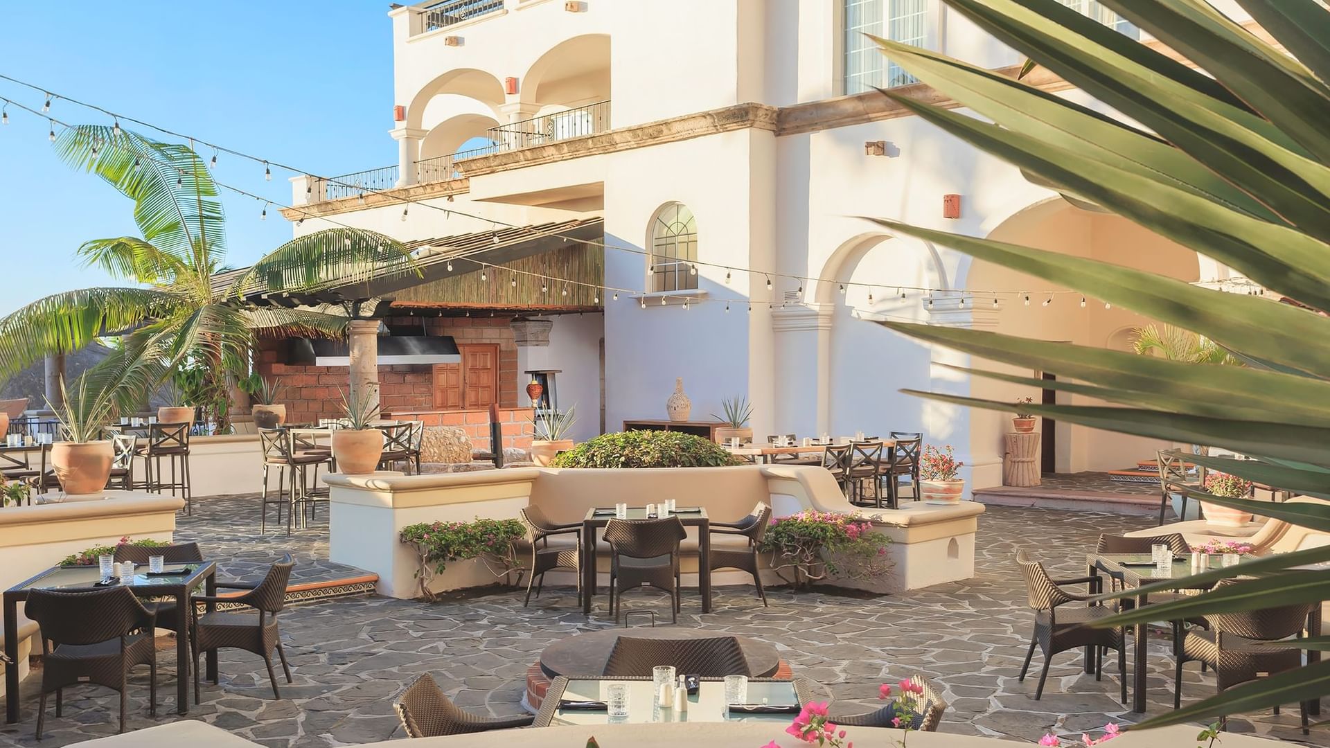 Tahona courtyard with stone flooring, empty dining tables, and a poolside bar at Hacienda del Mar Los Cabos.