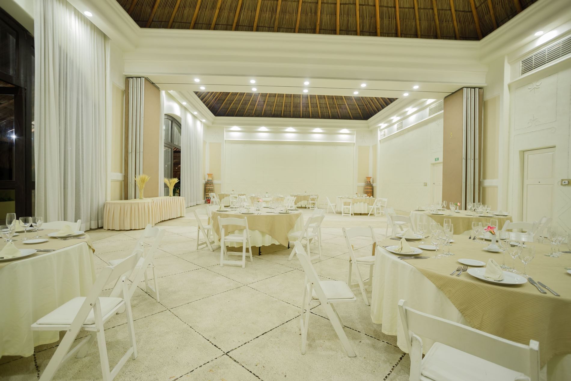 Elegant Ixtac Venue set with round tables, white chairs, and a high thatched roof at Quinta Real Acapulco