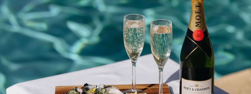 Bottle of Moët & Chandon champagne, two glasses, and oysters by the pool for a romantic escape.