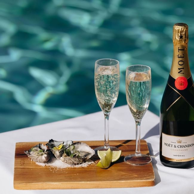 Bottle of Moët & Chandon champagne, two glasses, and oysters by the pool for a romantic escape.