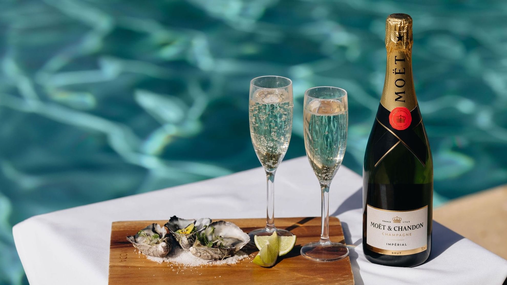Bottle of Moët & Chandon champagne, two glasses, and oysters by the pool for a romantic escape.