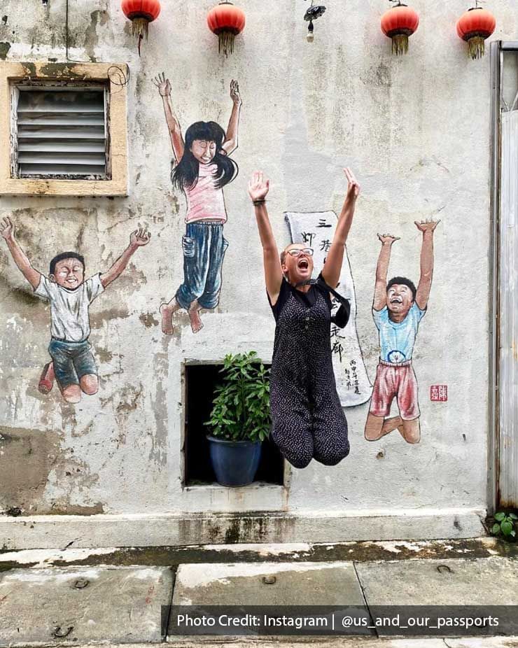 A lady was striking a jump pose and taking a picture with the Ipoh street art - Lexis Suites Penang