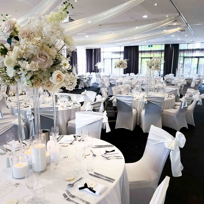 Banquet hall with white chairs, draped tables, floral centerpieces, and elegant decor ready for an event.