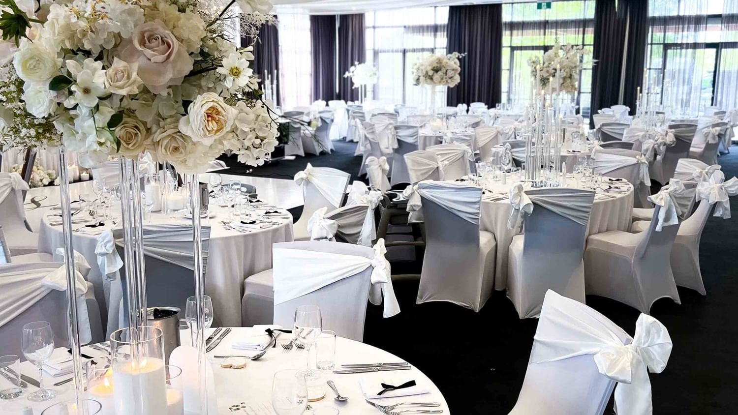 Banquet hall with white chairs, draped tables, floral centerpieces, and elegant decor ready for an event.
