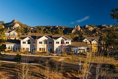 A large resort building nestled against a backdrop of trees and a mountain range at The Stanley Hotel