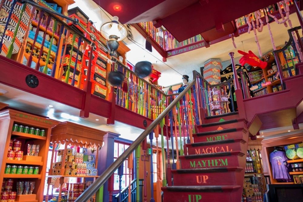 A colorful two-story interior with shelves of products and a rickety staircase leading up to a balcony.