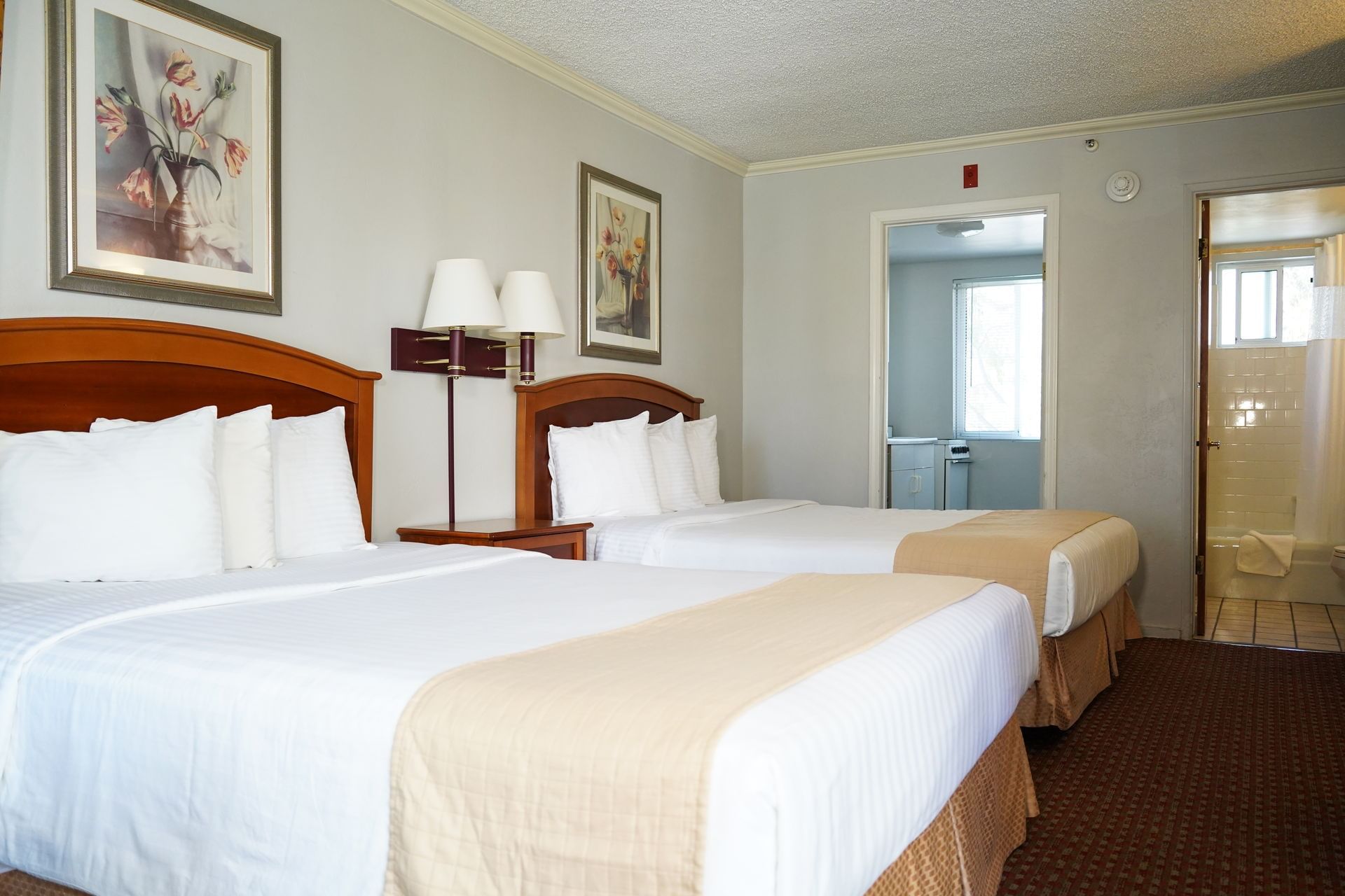 A hotel room with two beds, a nightstand, and a bathroom doorway.