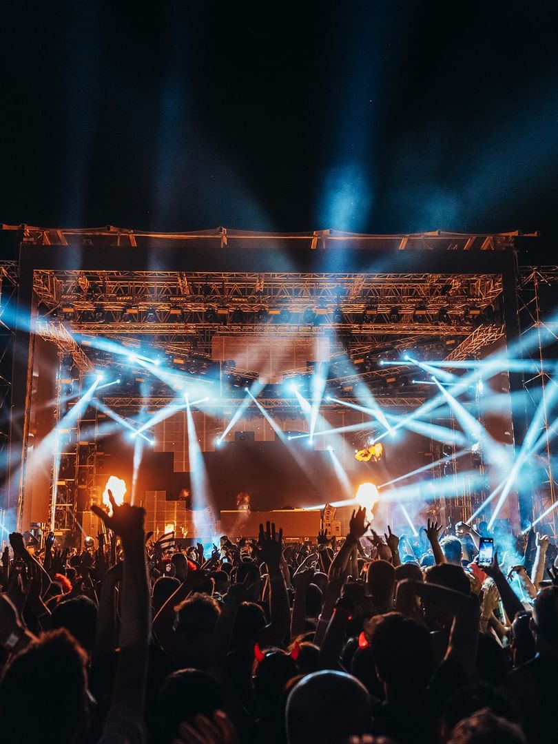 Energetic crowd enjoying a nighttime outdoor music festival with dramatic blue stage lighting and performers on stage
