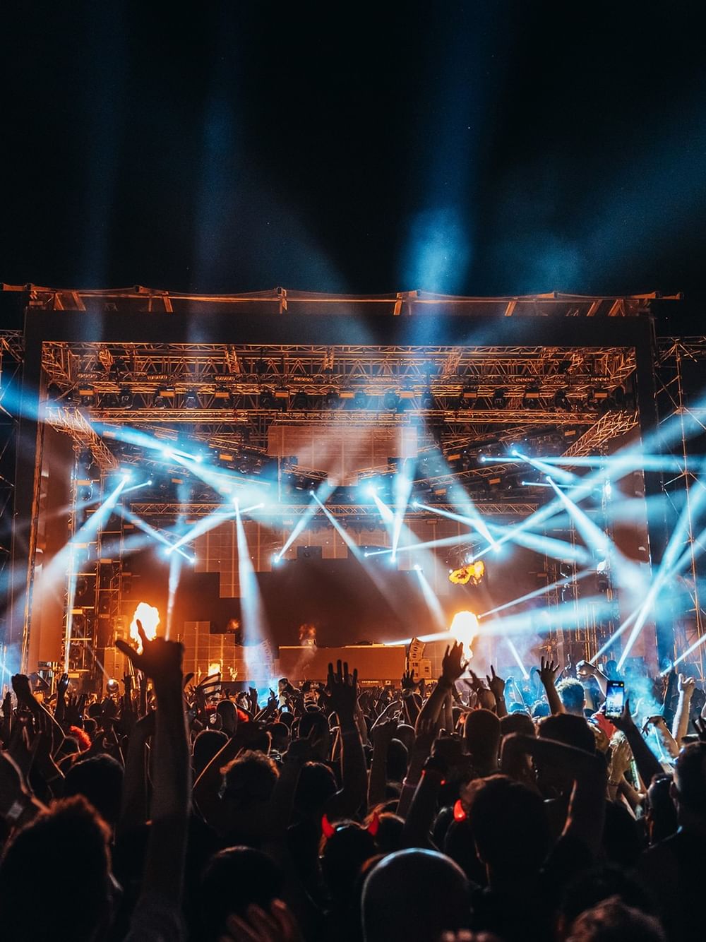 Energetic crowd enjoying a nighttime outdoor music festival with dramatic blue stage lighting and performers on stage