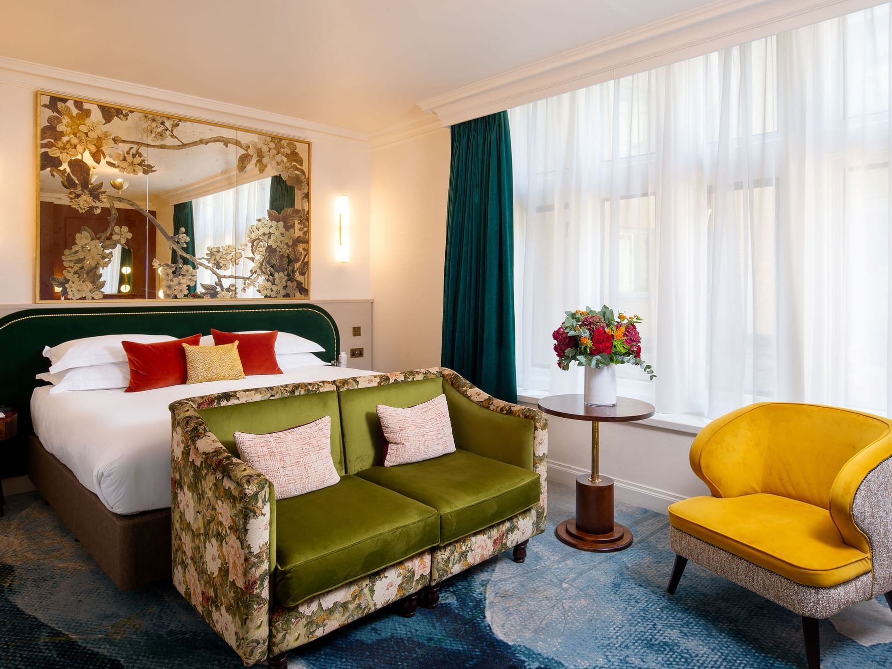 A bedroom with a large bed, floral couch, yellow chair, and vase of flowers by the window at Warwick Hotels and Resorts
