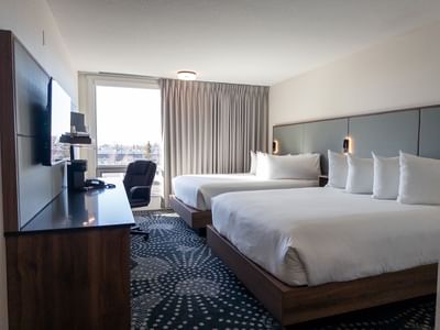 Hotel room with two beds, a desk, and a large window at Carriage House Hotel & Conference Centre