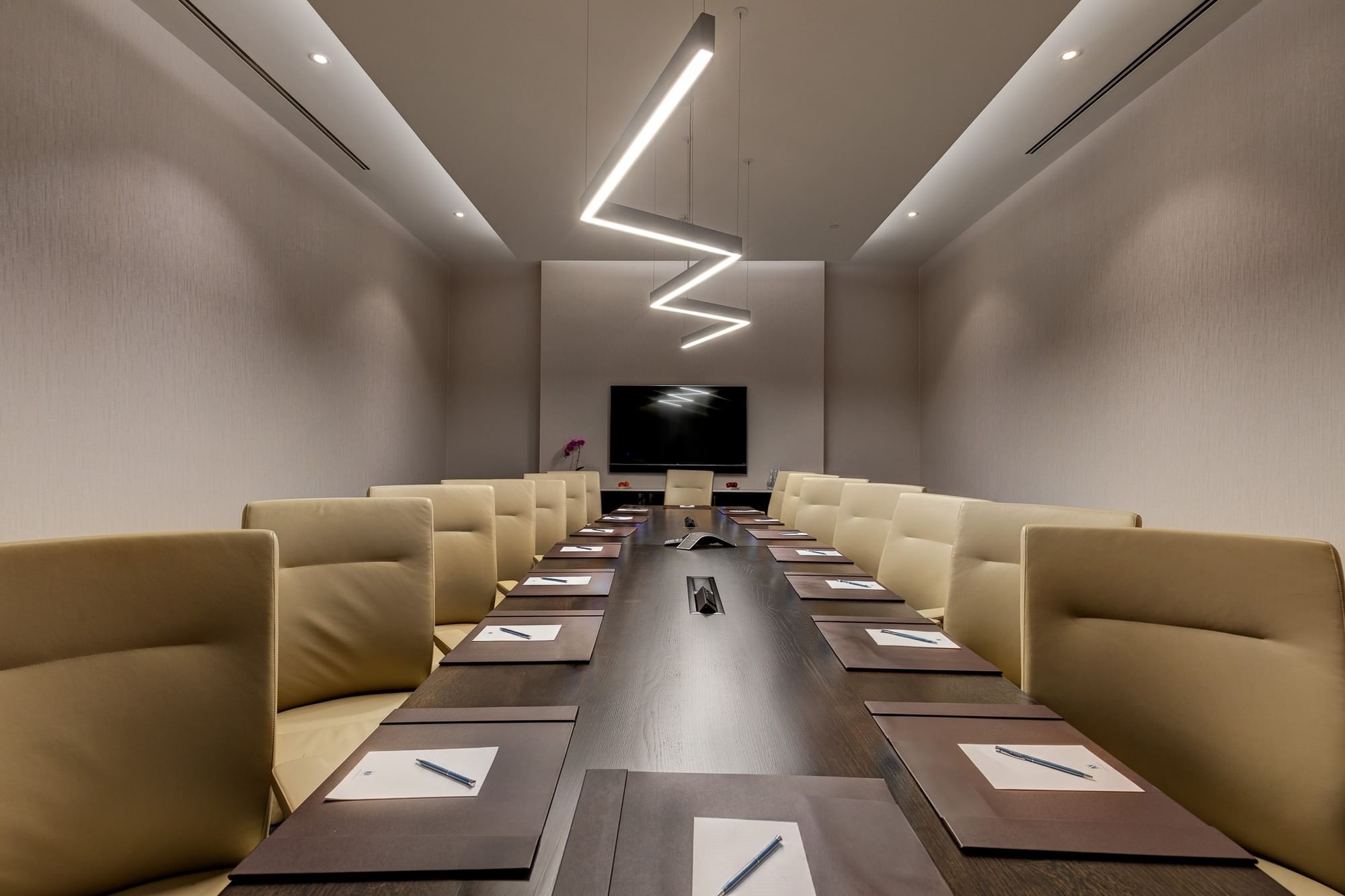 Cream leather chairs set by a dark wood table under zigzag pendant lighting in Champion\'s Boardroom at Hotel X Toronto