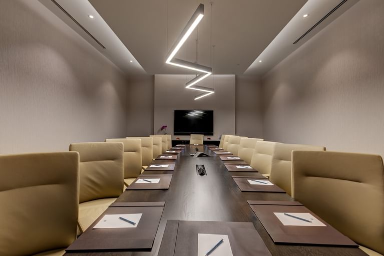 Cream leather chairs set by a dark wood table under zigzag pendant lighting in Champion\'s Boardroom at Hotel X Toronto