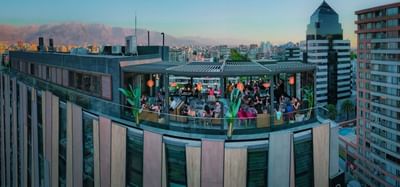 Rooftop Bar Vistandes bustling with diners, surrounded by cityscapes and mountains under a pastel sunset sky at Hotel Nodo