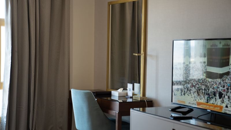 Desk with chair and large framed mirror next to TV at Saja by Warwick Madinah.