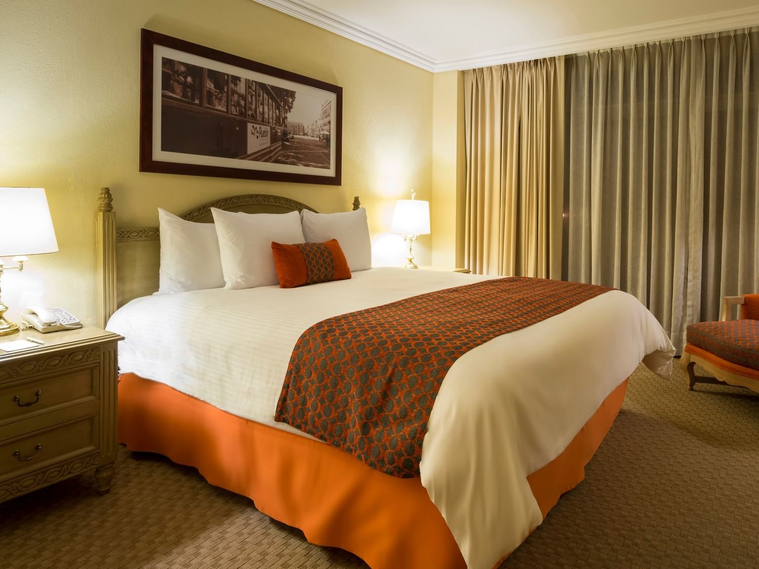 Master Suite King con cama king size, cortinas beige y sillón naranja en Camino Real Puebla Angelópolis