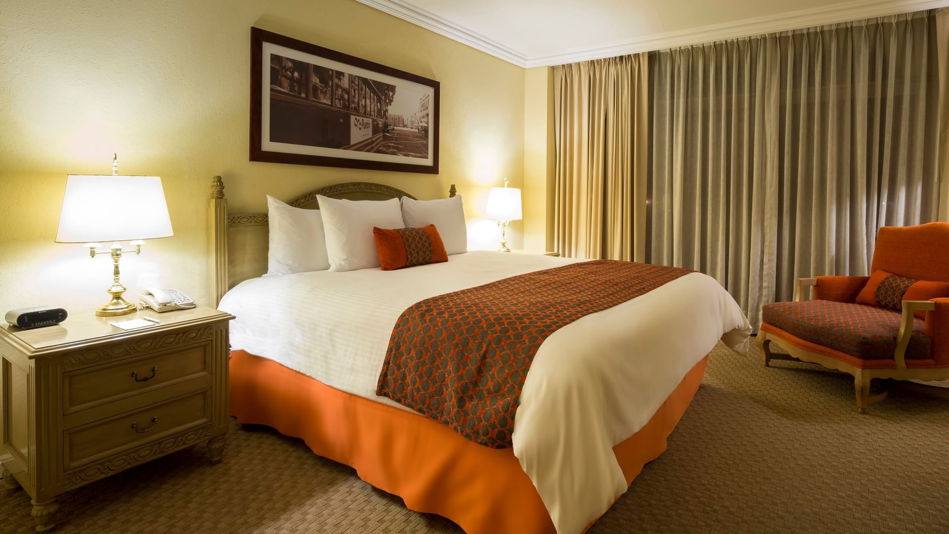 Master Suite King con cama king size, cortinas beige y sillón naranja en Camino Real Puebla Angelópolis
