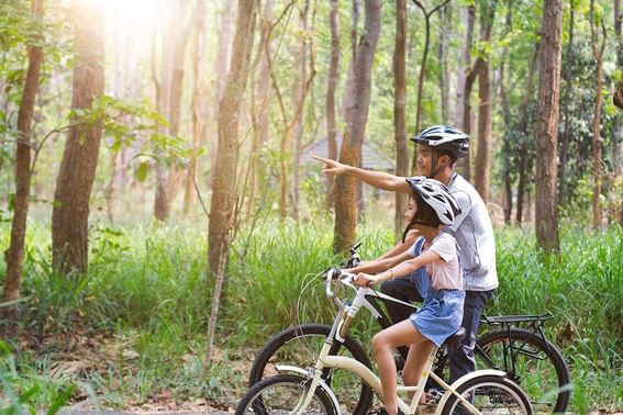 Two kids riding bicycles in a forest & one pointing forward near Grand Park Otaru