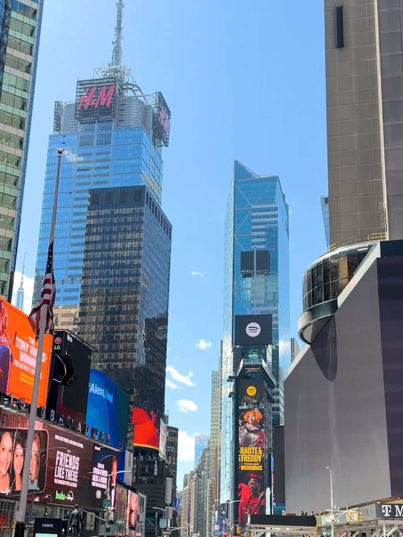 Times Square city street view with massive digital billboards by tall glass skyscrapers near Warwick Hotels & Resorts