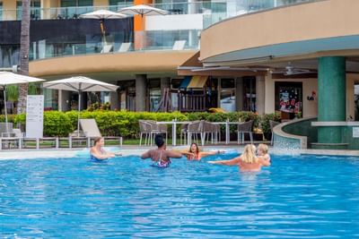 Grupo de personas disfruta hace gimnasia en la piscina al aire libre en el Sunset Plaza Beach Resort, uno de los mejores hoteles con vistas a la playa en Puerto Vallarta