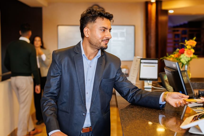 Man in a suit at a dark marble reception counter holding a key card in his hand at Rodd Royalty