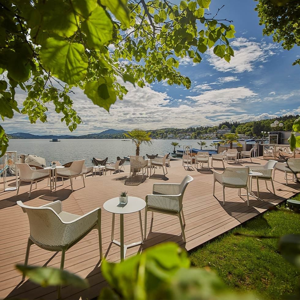 Terrazza esterna di un ristorante con vista sul lago e sedie bianche sotto un cielo parzialmente nuvoloso.
