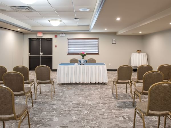 Chairs arranged in rows facing a small stage with a table and flowers in a meeting room.