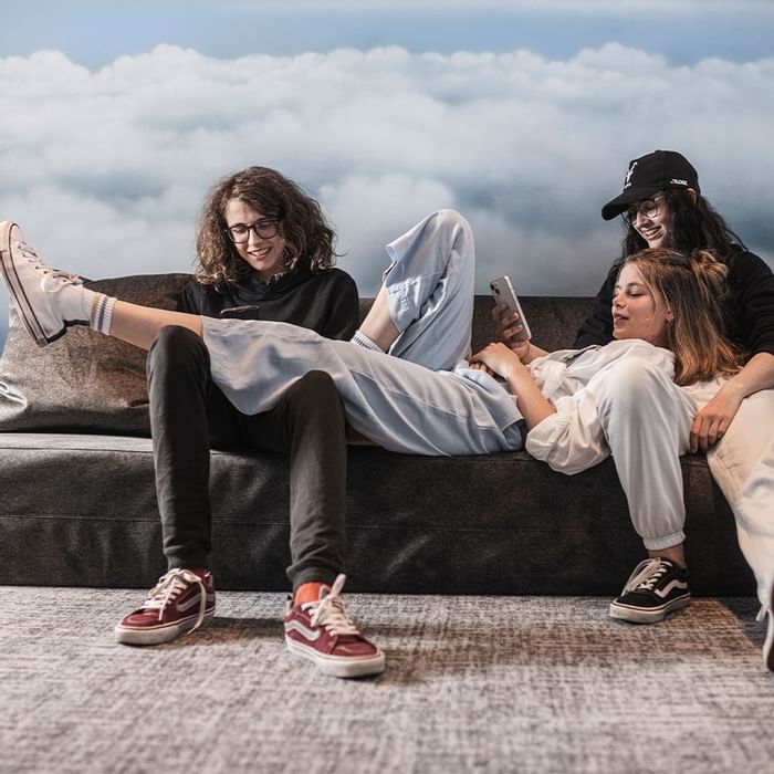 Tre amici si rilassano su un divano con smartphone, uno disteso sopra gli altri due.